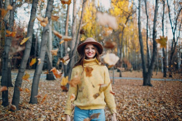 Modello di giovane donna nel parco autunnale con foglie di acero fogliame giallo Moda autunnale