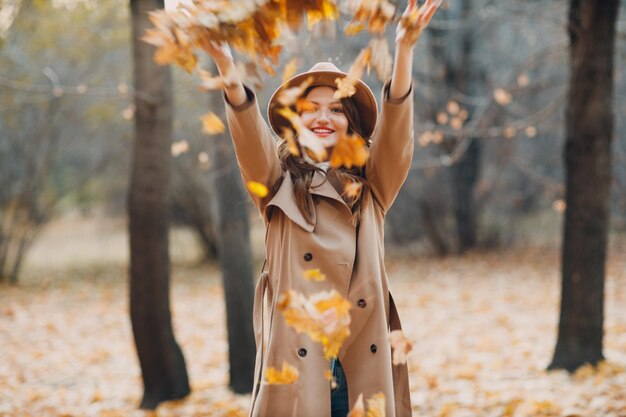 Modello di giovane donna nel parco autunnale con foglie di acero fogliame giallo Moda autunnale