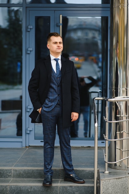 Modello di giovane uomo d'affari bello fiducioso elegante in abiti vestito che cammina per la strada.