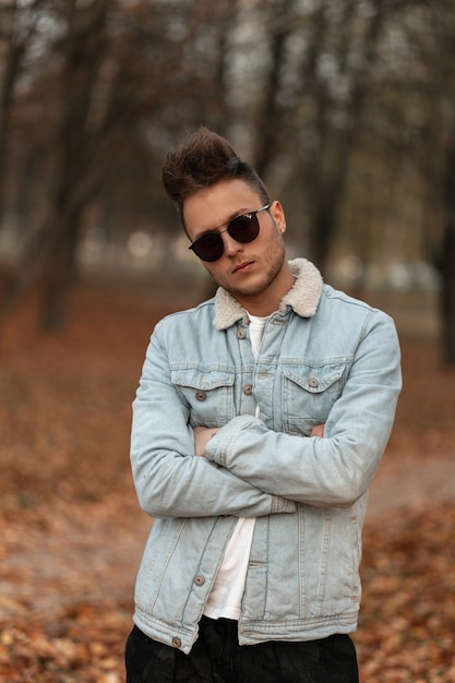 modello di giovane uomo in una giacca blu denim alla moda passeggiate nel parco