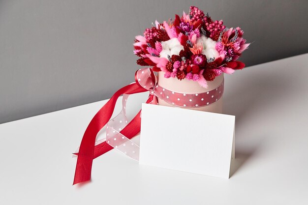 Modello di invito o biglietto di auguri e bouquet di fiori secchi sul tavolo bianco
