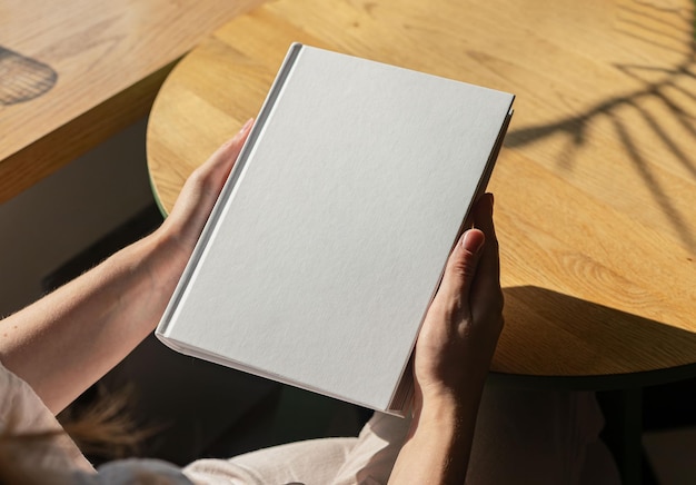 Modello di libro con la mano che tiene la copertina rigida su un tavolo di legno