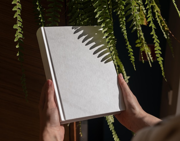 Modello di libro e pianta verde Copertina rigida pulita copertina chiara vuota in mano