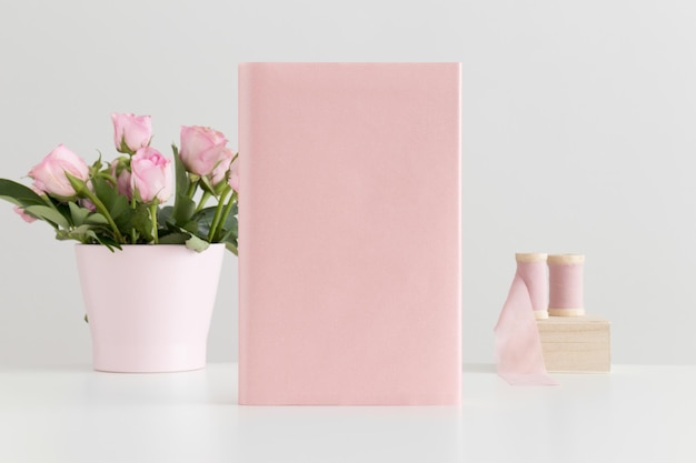 Modello di libro rosa con nastri di seta e rose rosa in una pentola su un tavolo bianco