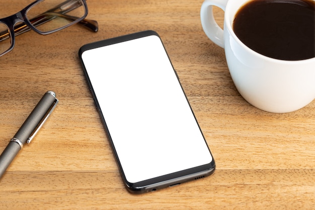 Modello di mockup di smartphone con tazza di caffè e occhiali sul tavolo di legno. Schermo bianco