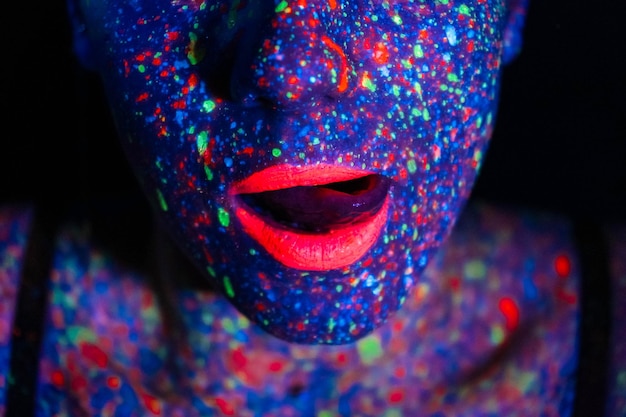 Modello di moda donna in luce al neon ritratto di una bellissima modella con trucco fluorescente body art design in faccia dipinta UV trucco colorato su sfondo nero di una ragazza Ballerina da discoteca in luce al neon