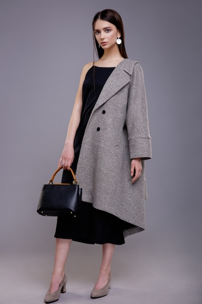 Modello di moda in cappotto grigio con borsa nera bella giovane donna Studio girato Sfondo grigio