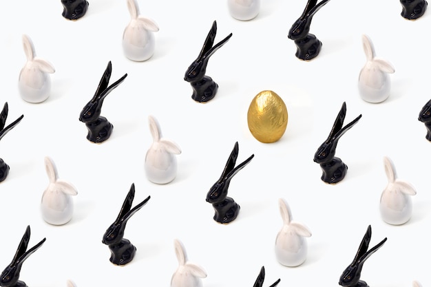 Modello di Pasqua alla moda fatto di giocattoli di lepri conigli bianchi e neri e uovo d'oro su sfondo isometrico