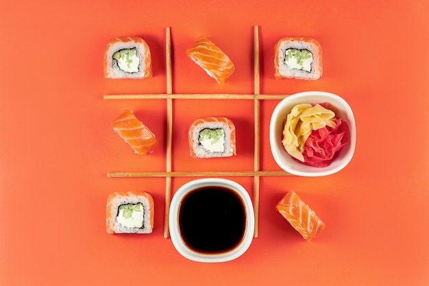Modello di rotoli di sushi Philadelphia con salmone su uno sfondo arancione. Il sushi è distribuito come in un gioco di tris