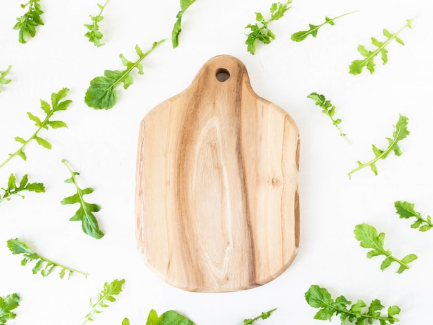 Modello di rucola isolato su sfondo bianco. Composizione fatta di foglie di rucola e tagliere di legno. Vista piana, vista dall'alto