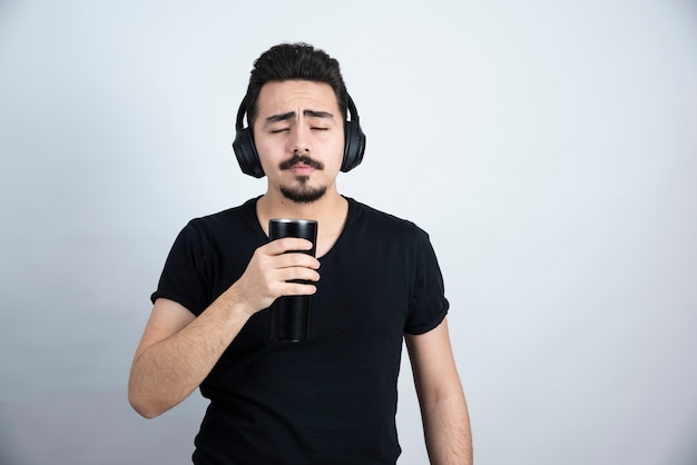 Modello di uomo castana in maglietta nera che tiene una tazza con gli occhi chiusi.