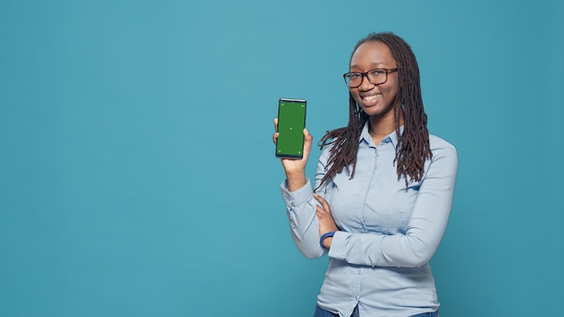 Modello femminile che tiene smartphone con display a schermo verde in studio che mostra il modello di mockup isolato