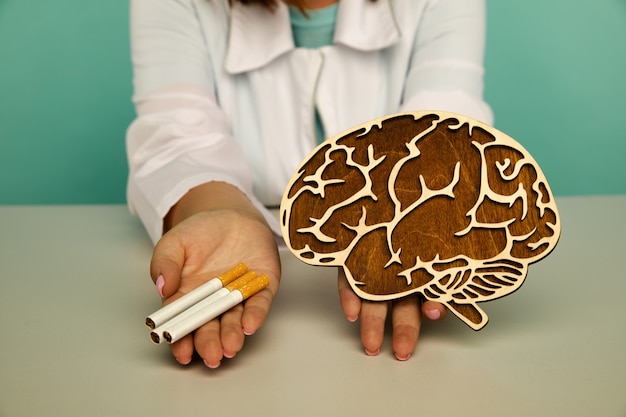 Modello in legno di cervello e sigaretta nelle mani di un'infermiera che fuma dipendenza