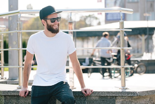 Modello maschio bello hipster con barba che indossa t-shirt bianca vuota con spazio per il tuo logo o design in stile urbano casual