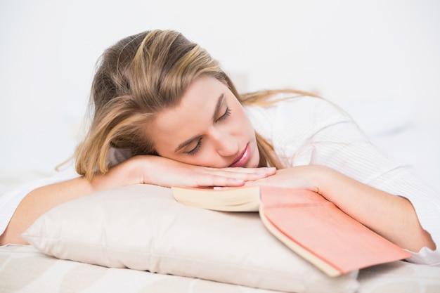 Modello splendido che dorme sul letto accogliente con il libro accanto