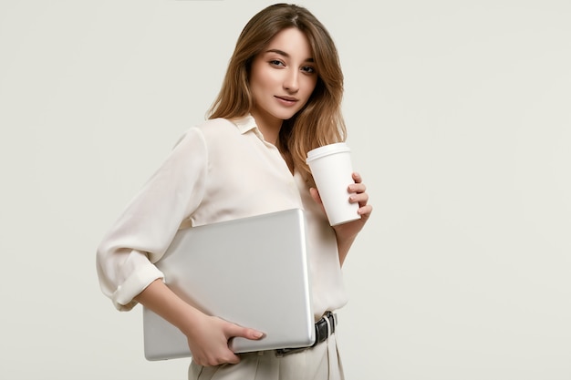 Modello splendido del brunette in vestiti bianchi con il computer portatile e il caffè