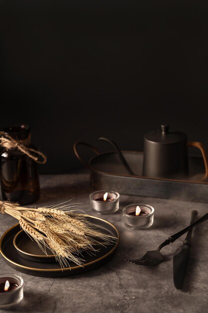 modello vintage con vecchie stoviglie in metallo orecchio di grano e candele accese su sfondo di pietra nera per il concetto di progettazione concetto di autunno concetto di design d'interno