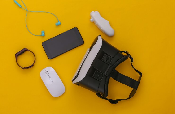 Modern gadgets and devices. Virtual reality headset with smartphone, controller, earphones, smart bracelet, pc mouse on yellow background. Top view. Flay lay