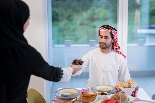 moderna famiglia musulmana multietnica che condivide una ciotola di datteri mentre si gusta la cena iftar insieme durante una festa del Ramadan a casa.