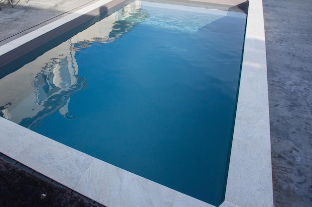 Moderna piscina domestica con rivestimento in pietra con terrazza in cemento cerato grigio e acqua blu trasparente