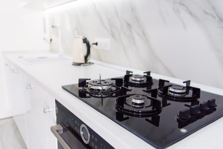 Moderna stufa a gas nera high-tech con pannello sensore nel luminoso interno della cucina con piastrelle in marmo bianco.