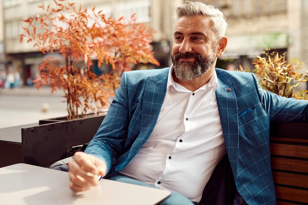 Moderno uomo d'affari anziano che fuma una sigaretta mentre riposa in un caffè dopo una dura giornata di lavoro.