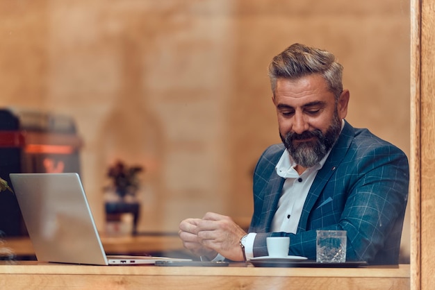 Moderno uomo d'affari senior seduto al bar e utilizzando laptop e smartphone.