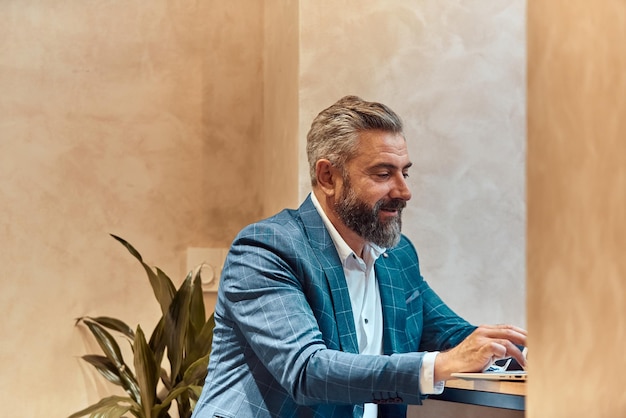 Moderno uomo d'affari senior seduto al bar e utilizzando laptop e smartphone.