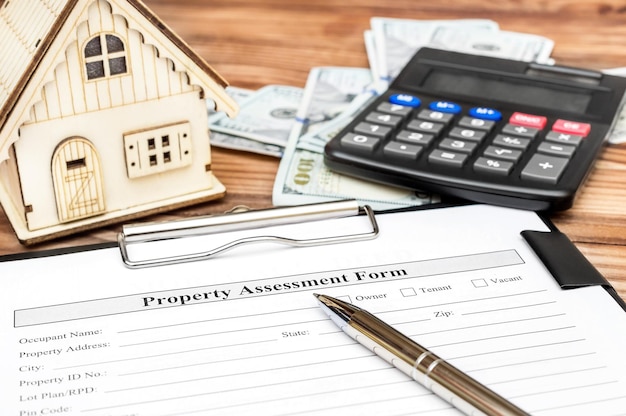 Modulo di valutazione della proprietà con calcolatore di denaro e modello di casa sul tavolo Concetto di valutazione della proprietà