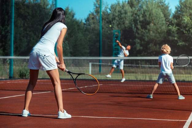 Moglie dai capelli scuri che gioca a tennis con marito e figlio