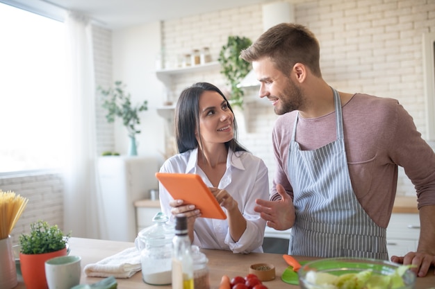 Moglie sorridente attraente che tiene compressa arancione mentre cucina con il marito