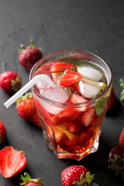 Mojito alla fragola. Cocktail mojito estivo freddo con fragole, menta, limone e ghiaccio in un bicchiere su un tavolo nero. su uno sfondo scuro