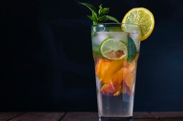 Mojito alla pesca in un bicchiere trasparente con ghiaccio su sfondo scuro