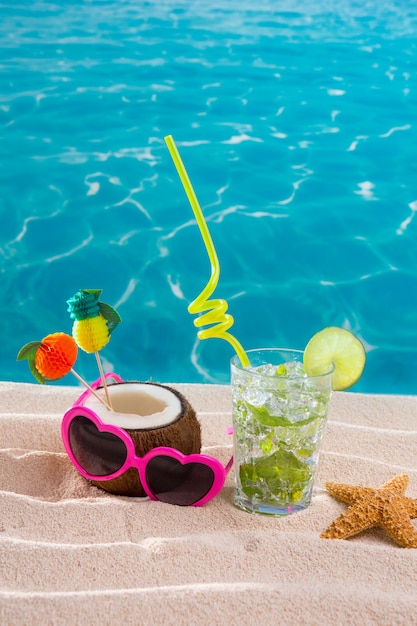 Mojito cocktail sulla spiaggia di sabbia con cocco e occhiali da sole