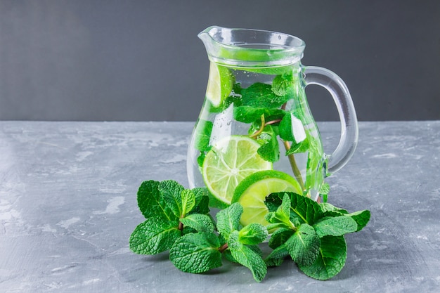 Mojito con menta e lime in un bicchiere e una brocca con tubi. Sfondo di marmo grigio.