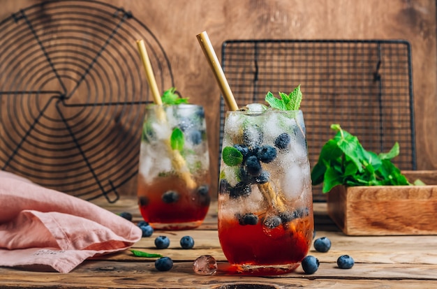 Mojito di ghiaccio al mirtillo con menta in bicchieri alti su fondo di legno rustico.