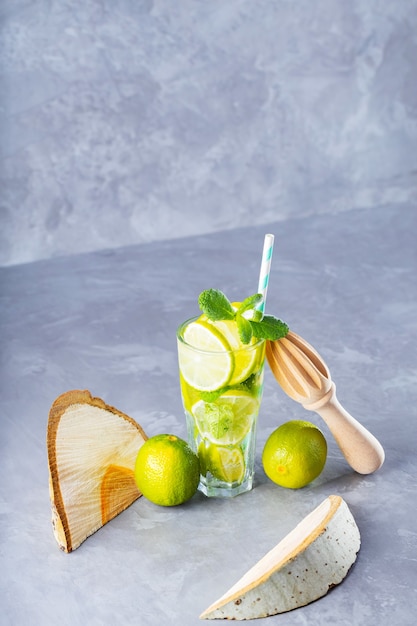 Mojito in bicchiere con lime, menta fresca e ghiaccio. Mojito cocktail estivo, pezzi di legno e spremiagrumi manuale su sfondo grigio. Composizione creativa