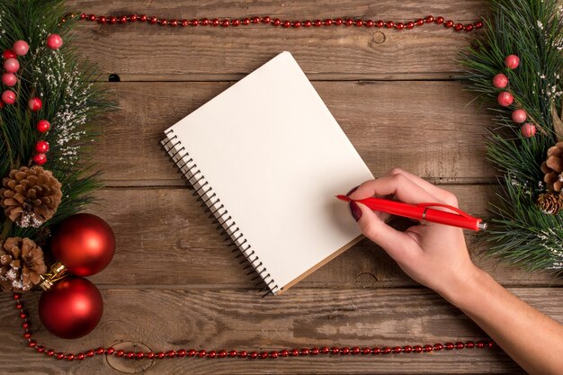 Mokcup di Capodanno e Natale. scrittura a mano su un notebook con luci di Natale su sfondo di legno, spazio per il testo, copyspace. da sopra. Concetto di pianificazione delle vacanze invernali. Stile piatto.