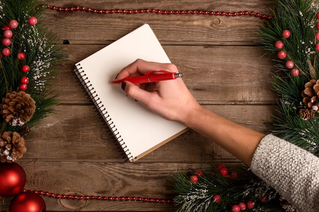 Mokcup di Capodanno e Natale. scrittura a mano su un notebook con luci di Natale su sfondo di legno, spazio per il testo, copyspace. da sopra. Concetto di pianificazione delle vacanze invernali. Stile piatto.