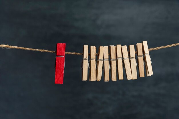 Mollette di legno sulla corda e una rossa. Differenza dagli altri. Separato dalla folla. Concetto di direzione.