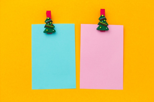 Mollette festive di Natale e fogli di carta bianca rosa e blu con spazio libero per il testo su uno sfondo giallo vibrante