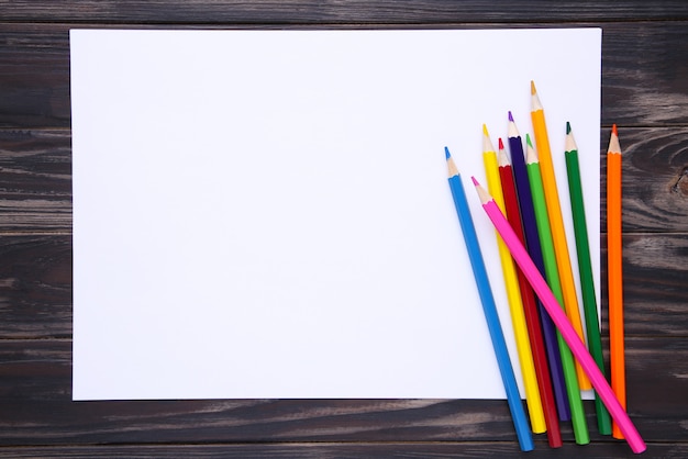 Molte matite colorate differenti con Libro Bianco su di legno marrone