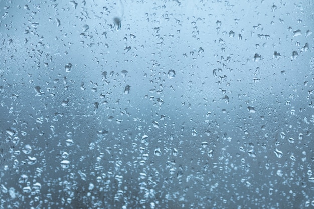 Molte piccole gocce di superficie di vetro d'acqua, finestra nelle gocce di pioggia, specchio nelle gocce di acqua di condensa di colore blu brillante.