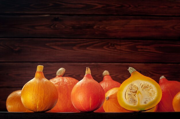 Molte piccole zucche arancioni e gialle nella parte inferiore del telaio su uno sfondo di tavole marroni. Una zucca viene tagliata. I semi sono visibili all'interno. Messa a fuoco selettiva sulle prime tre zucche.