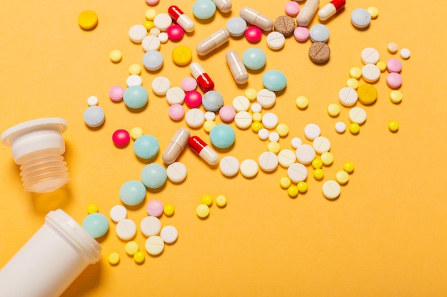 Molte pillole e capsule multicolori su uno sfondo arancione come concetto di dipendenza da medico