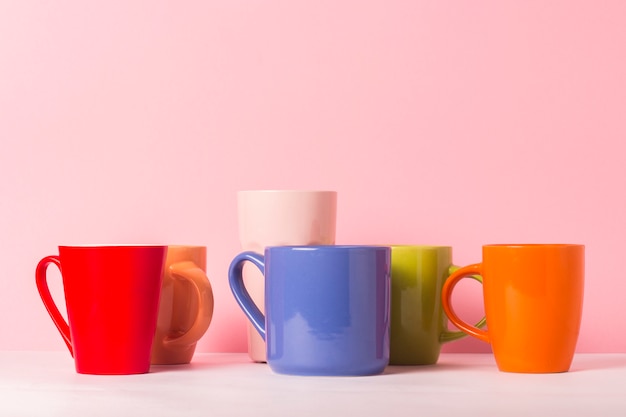 Molte tazze di caffè o tè multicolori su un fondo rosa. Il concetto di compagnia amichevole, famiglia numerosa, incontro di amici per una tazza di tè o caffè.