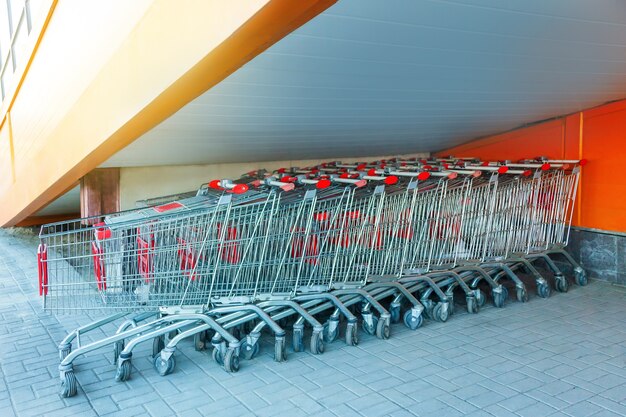 Molti carrelli della spesa in metallo su un parcheggio vicino al supermercato all'aperto, in piedi sotto le scale