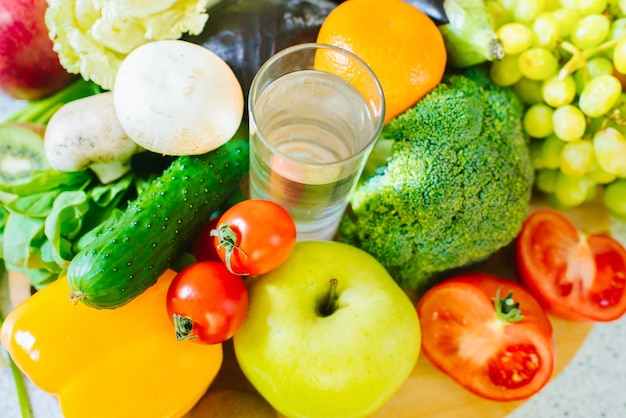 Molti diversi tipi di frutta e verdura con un bicchiere d'acqua nel mezzo