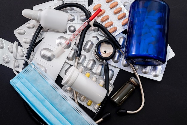 Molti farmaci stetoscopio pillole maschera siringhe gocce giacciono su uno sfondo nero Concetto di medicina