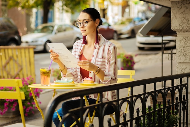 Molti pasti. Calma donna attenta guardando il menu e si prepara a mangiare il suo delizioso dessert in un caffè